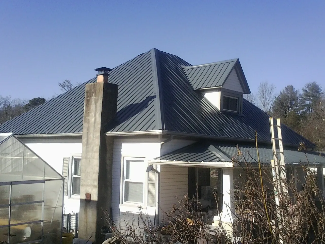 Dark blue standing seam metal roof on a white farmhouse with dormer — Slate & Tile Roof Repair by Roofing Brothers in Minburn