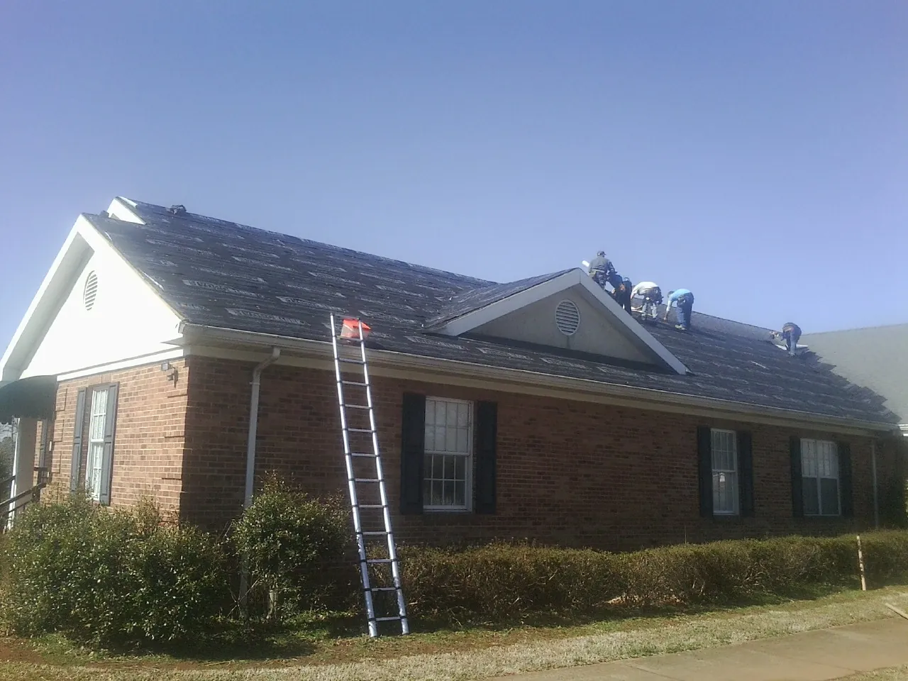 Crew tearing shingles off a brick ranch roof with a ladder set — Emergency Roof Repair work by our crew in Minburn