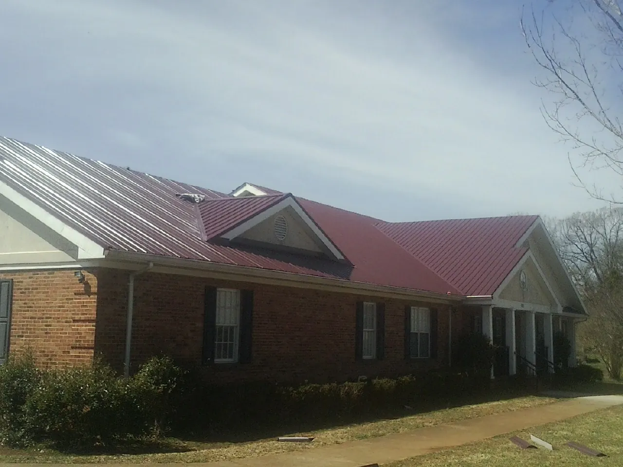 Red metal roof with gabled entries on a long brick building, from a Hail Damage Roof Repair job in Minburn