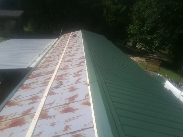 Old rusted panels beside newly installed green metal roofing — Wind Damage Roof Repair by Roofing Brothers in Minburn