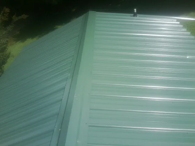 New green metal panels meeting at the ridge of a roof — Flat Roof Repair work by our crew in Minburn