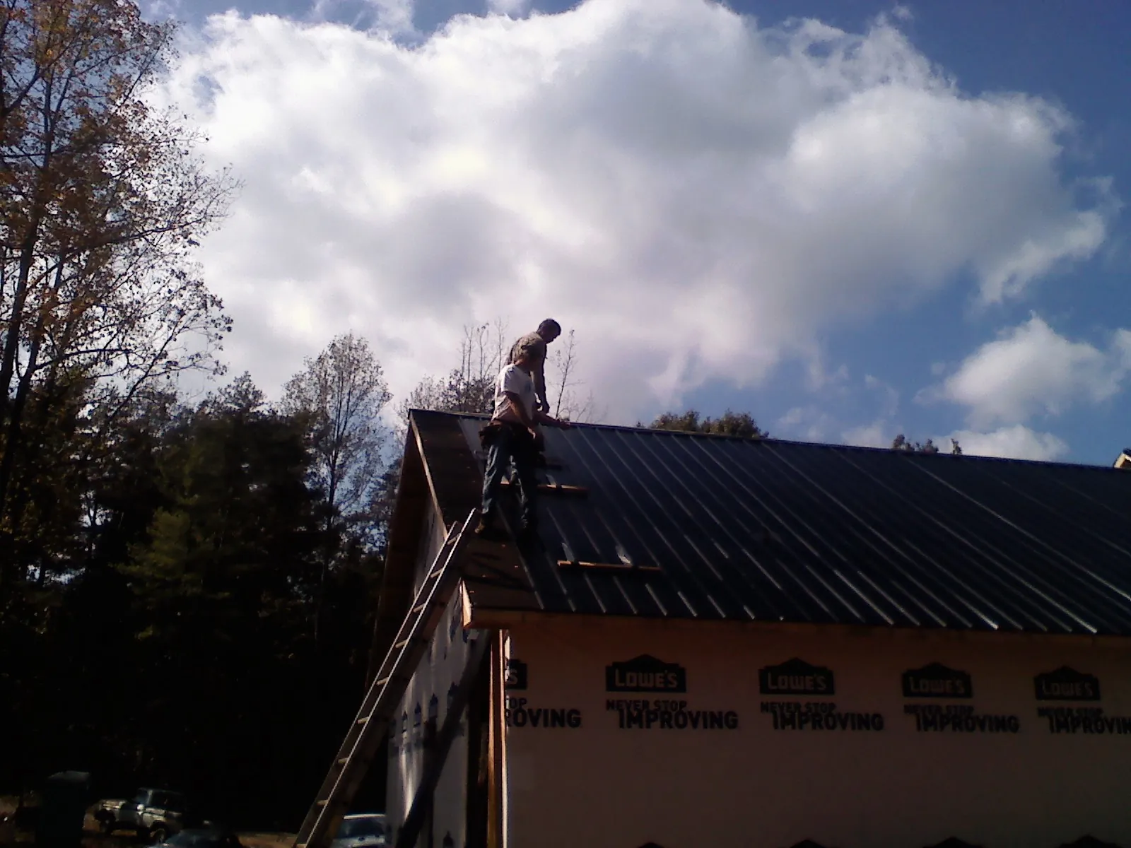 Roofer fastening dark metal panels high against a cloudy sky, from a Roof Inspection job in Minburn