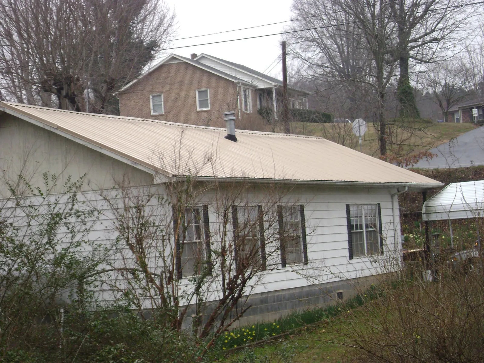 Tan metal roof on a white sided house set into a hillside — Commercial Roofing by Roofing Brothers in Minburn