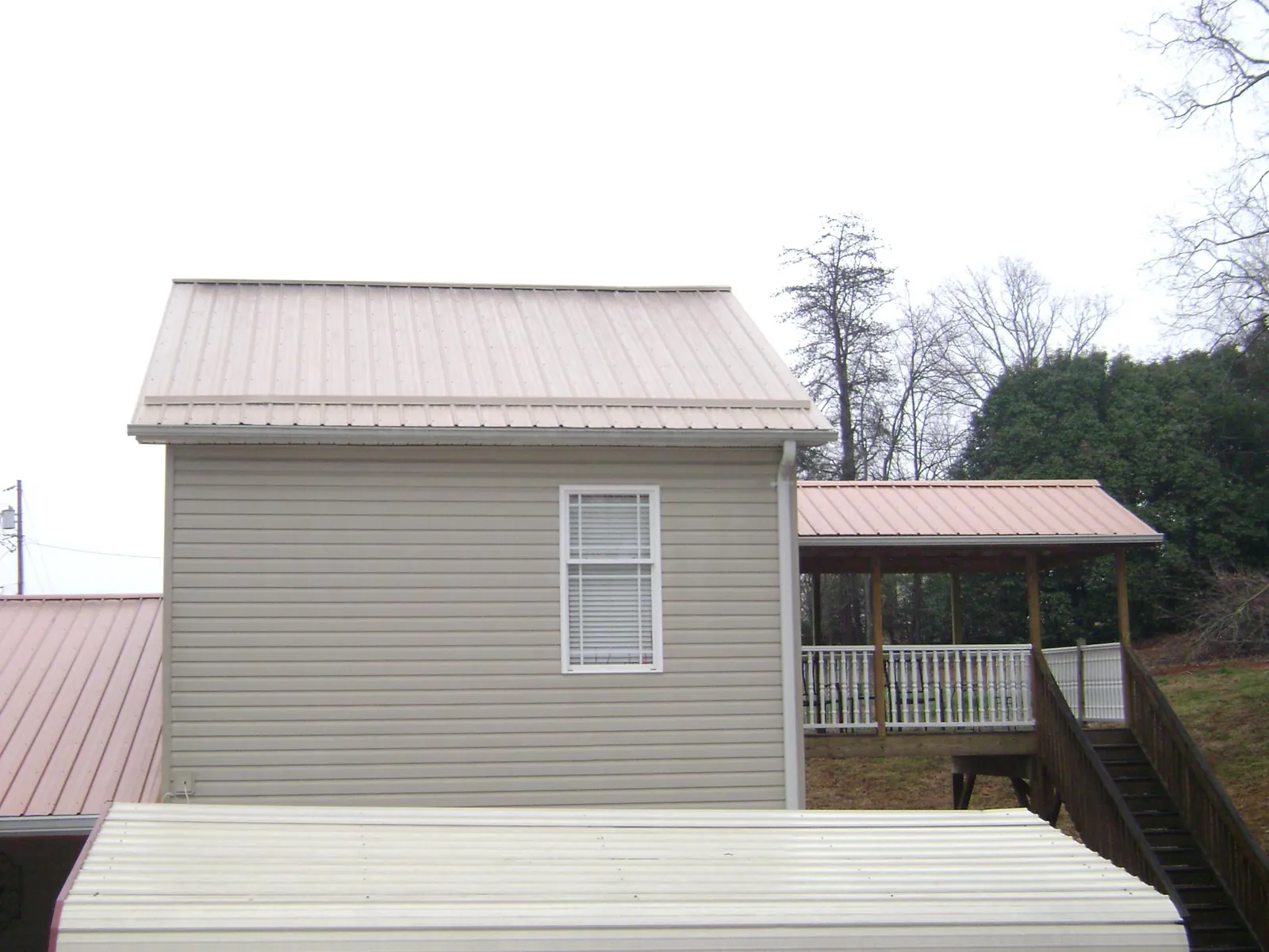 Tan metal roofs on a two story addition and attached porch, from a Roof Replacement job in Minburn